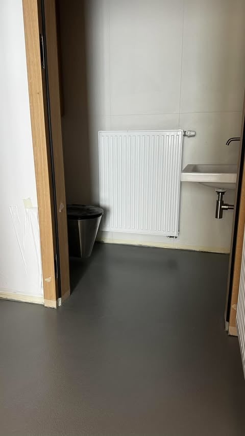 Pusta łazienka z białym grzejnikiem, umywalką i ciemnoszarą posadzką