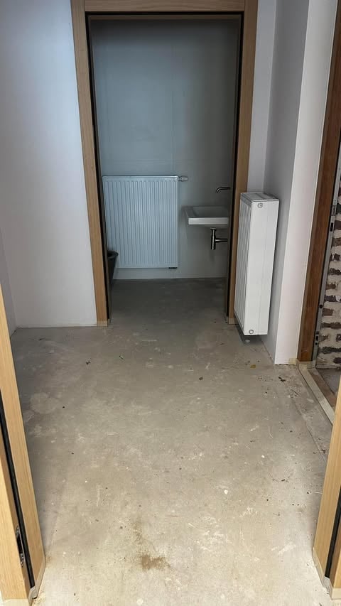 Puste pomieszczenie w trakcie remontu z betonową posadzką i drewnianymi ościeżnicami